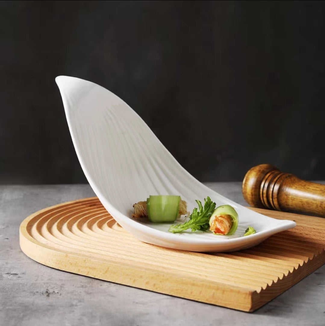White leaf-shaped ceramic plate with minimalist design and high-gloss finish, displayed on table with food plating.