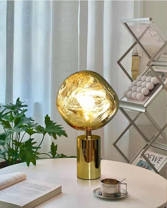 Molten glass globe table lamp with gold base styled on a minimalist desk.