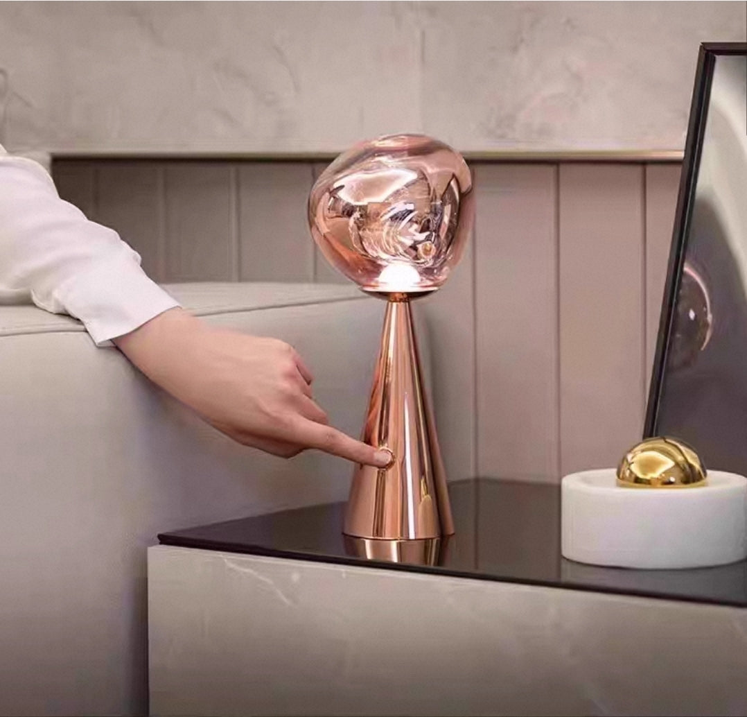 Artistic molten glass table lamp with chrome and gold variants in creative workspace.