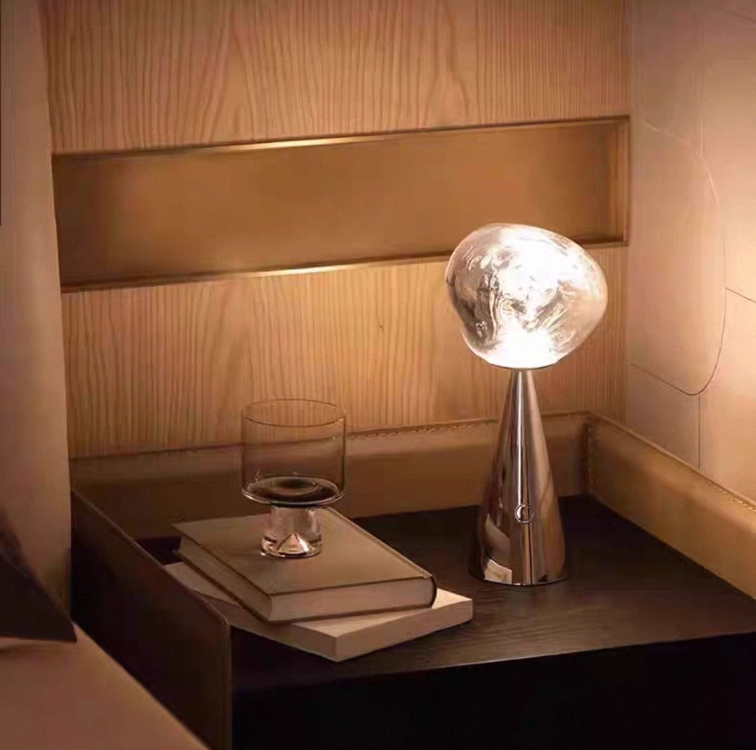 Modern table lamp on a nightstand with a glass and book in a softly lit room.