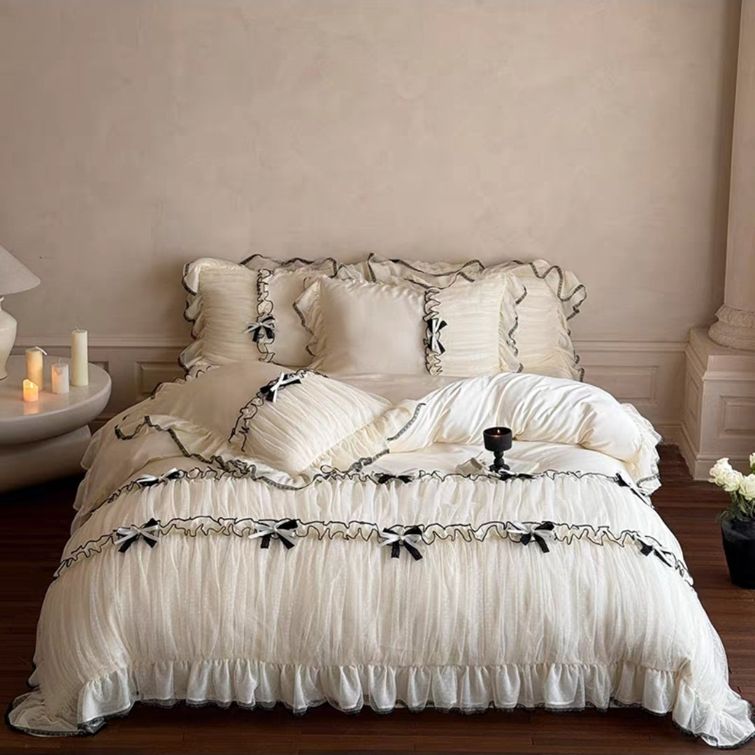 White ruffled bedding set on a bed with decorative pillows and candles on a nightstand.