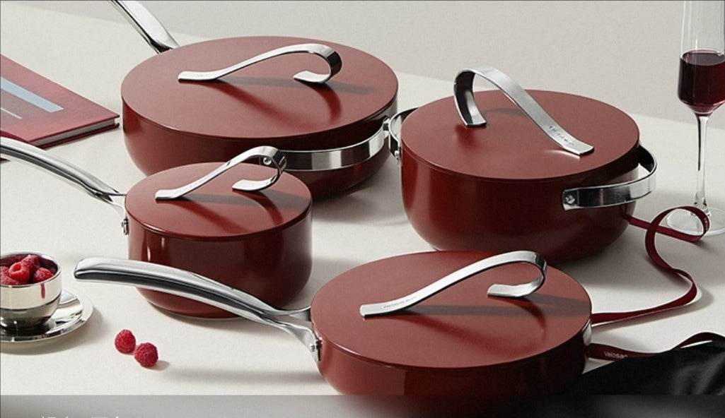 Set of red non-stick ceramic cookware with silver handles on a white surface.