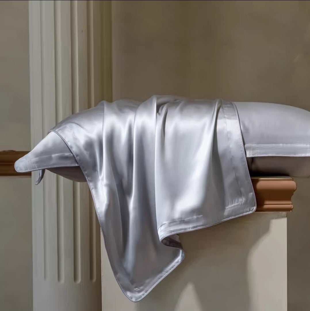 Silky silver blanket draped over a wooden chair against a neutral wall.