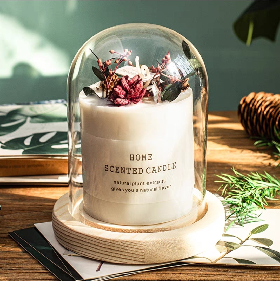 Home dried flower candle -scented with decorative elements under a glass dome on a wooden surface.