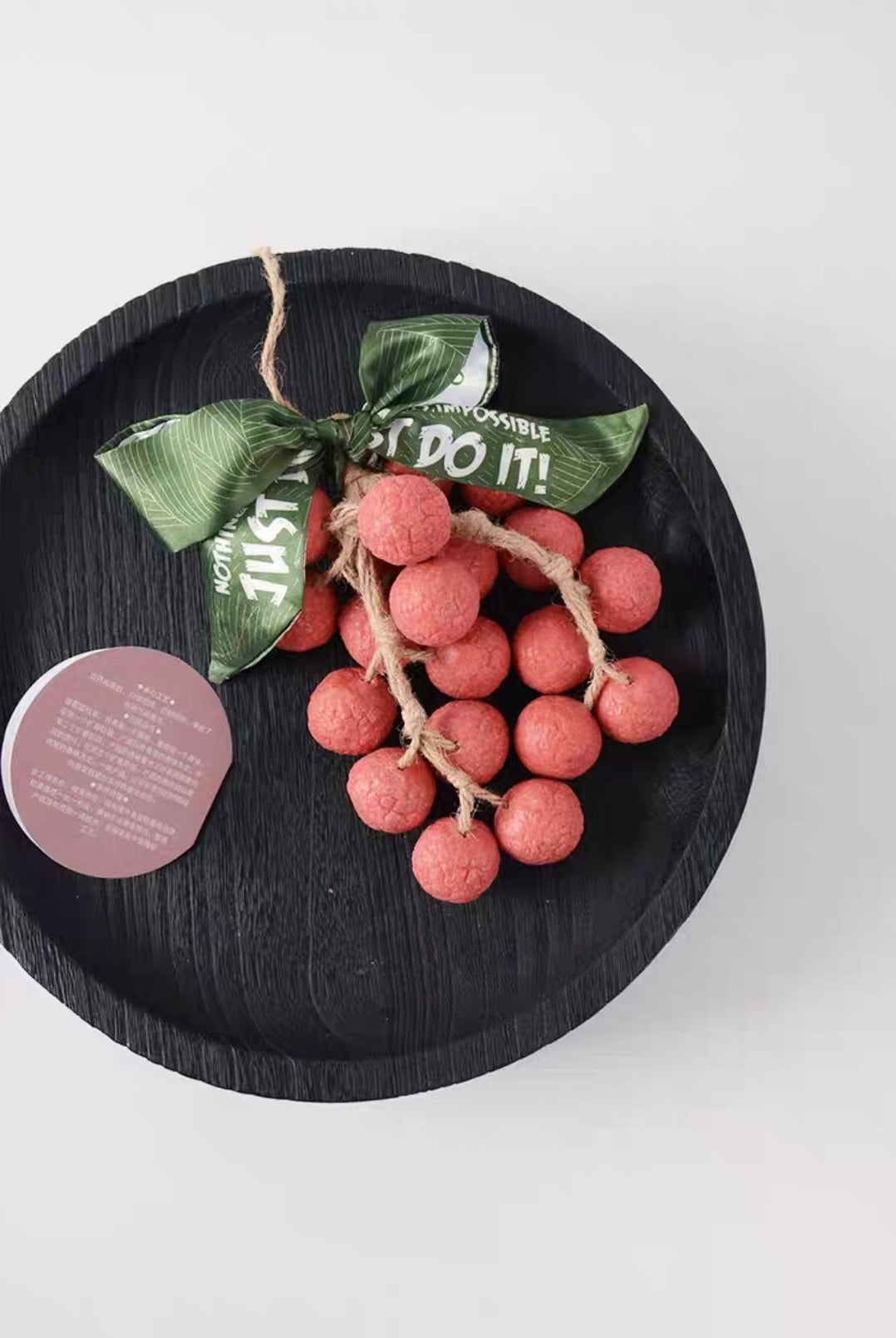 Decorative wreath with pink berries on a black plate against a white background