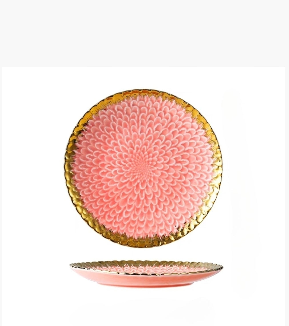 Pink ceramic plate with gold decorative rim on a white background