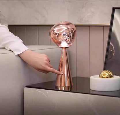 Artistic molten glass table lamp with chrome and gold variants in creative workspace.

