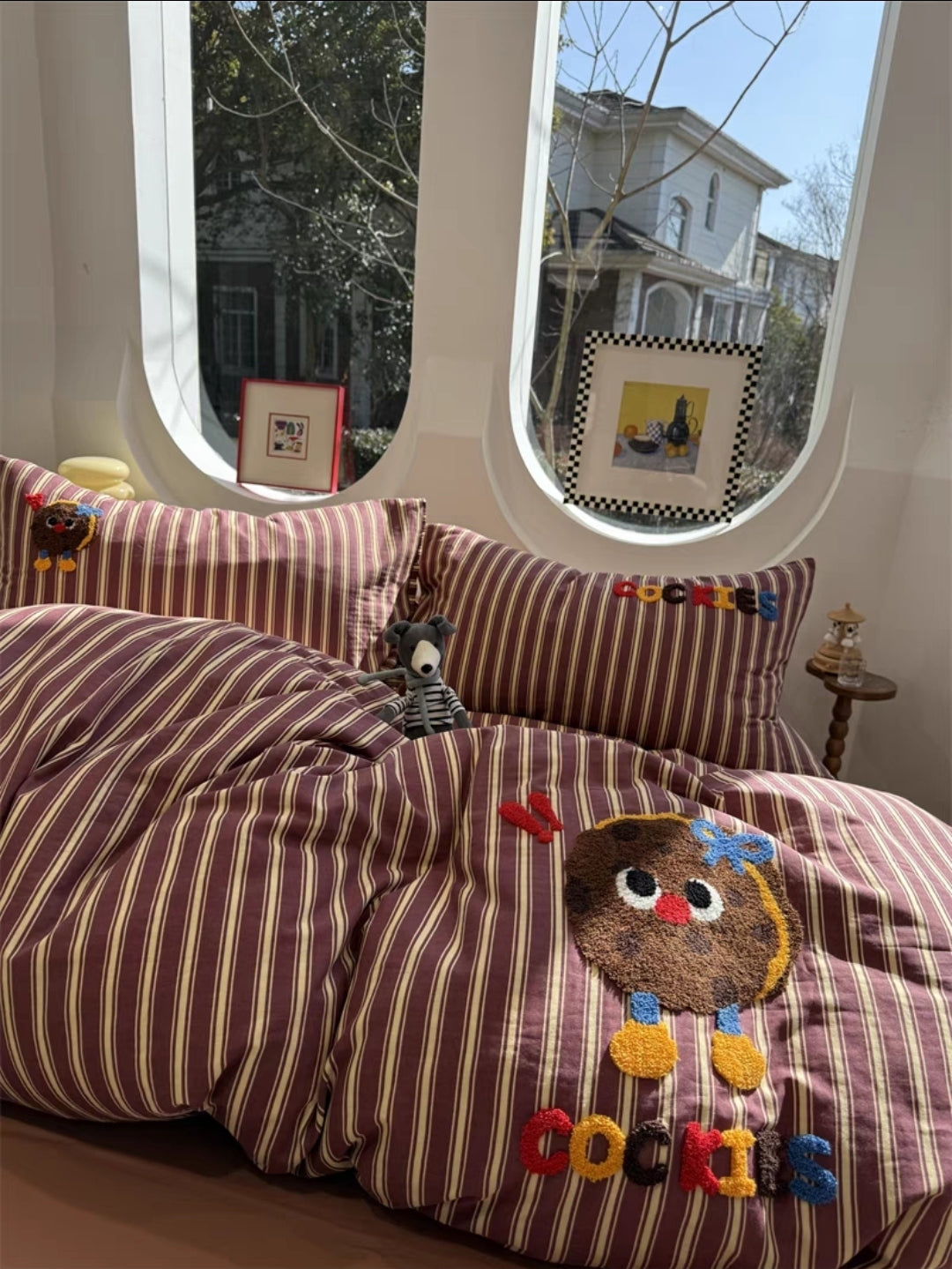 Striped bedspread with cartoon character and 'Cookies' text in a room with large windows.