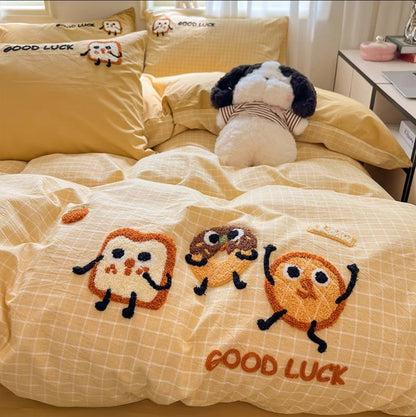 Yellow bedding set with cartoon characters and 'Good Luck' text on a bed.