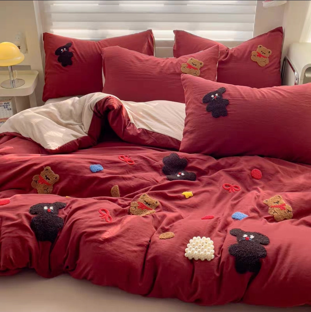 Red bedspread with teddy bear and flower patterns on a bed.