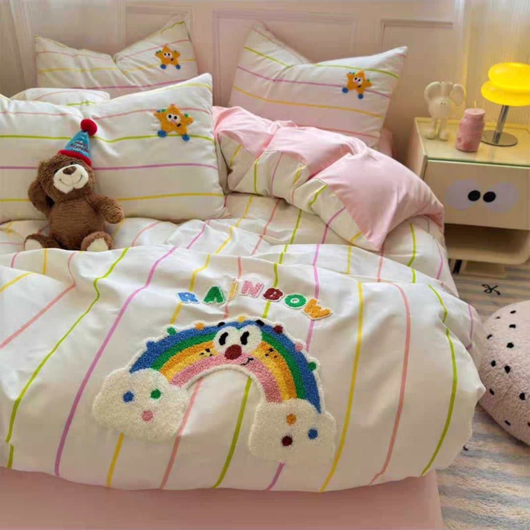Children's bedroom with colorful bedding featuring a rainbow and cartoon characters, teddy bear, and nightstand.